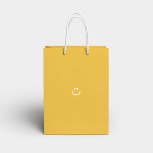 Yellow background with white image of eyes and a smile in middle of bag with white handles.  