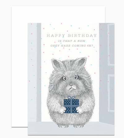 White card with confetti specks and gray text saying," Happy Birthday Is That A New Gray Hare Coming In?" Image of a gray bunny holding a blue birhday present. A white envelope is included.