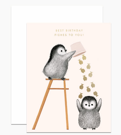 Light pink card with gold foil text saying, "Best Birthday Fishes To You!"  Images of a penguin standing on a ladder dumping a bucket of gold fish on another penguin's head. An ivory envelope is included.