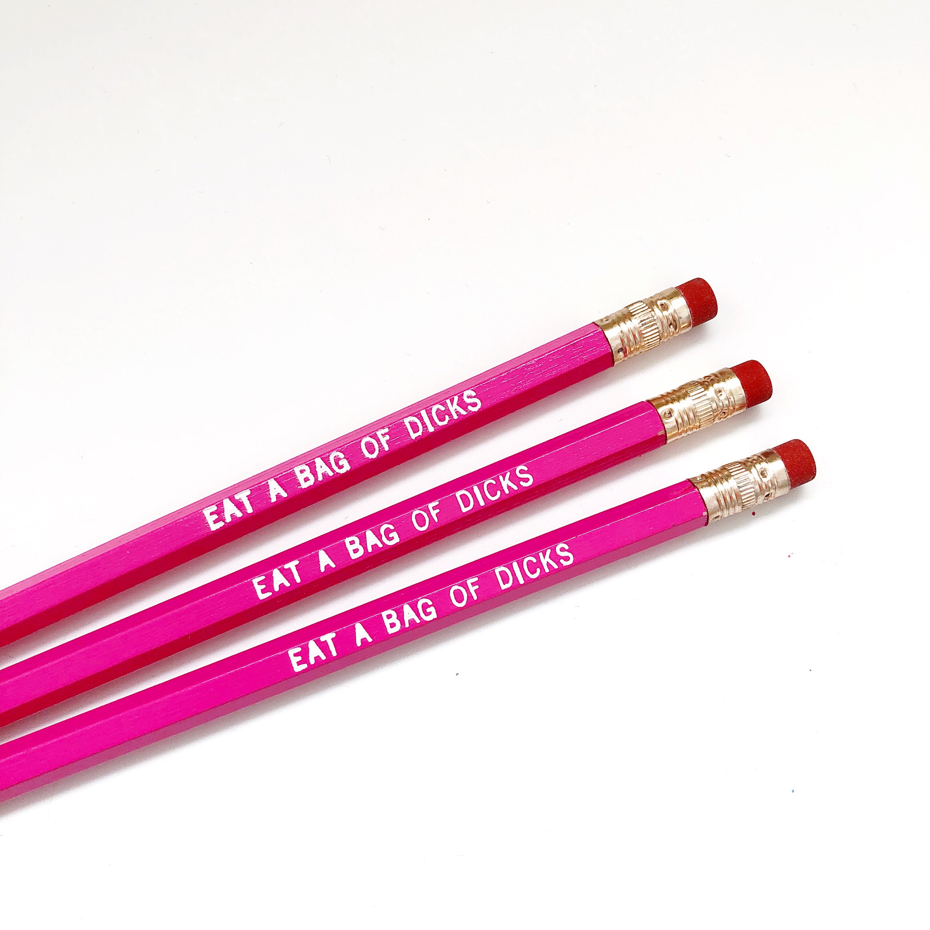 Image of three hot pink pencils with white text says, "Eat a bag of dicks". 