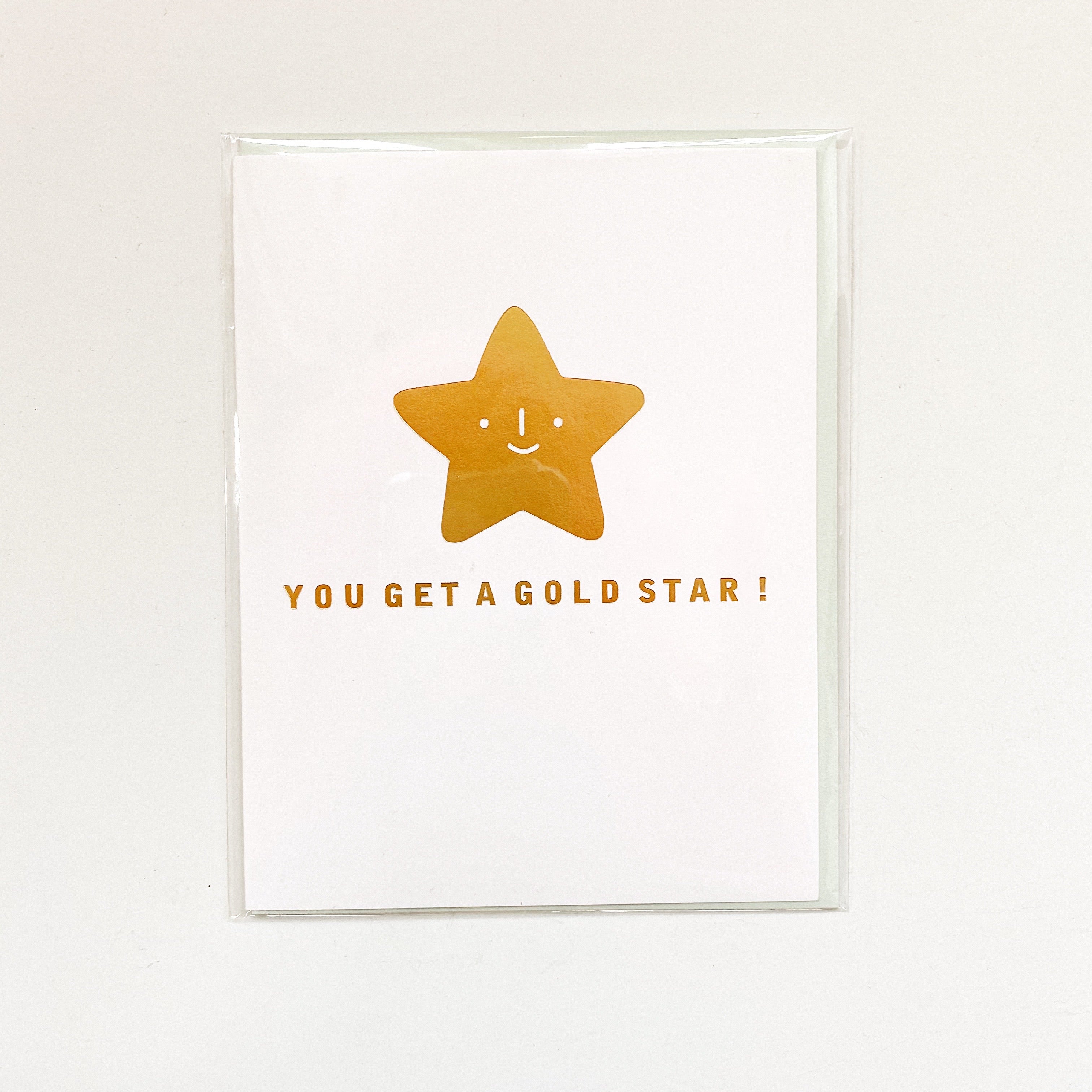 White card with gold foil text saying, “You Get a Gold Star!” Image a smiling gold foil star in center of card. An envelope is included.