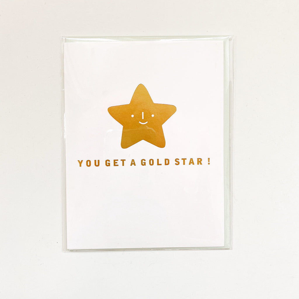 White card with gold foil text saying, “You Get a Gold Star!” Image a smiling gold foil star in center of card. An envelope is included.