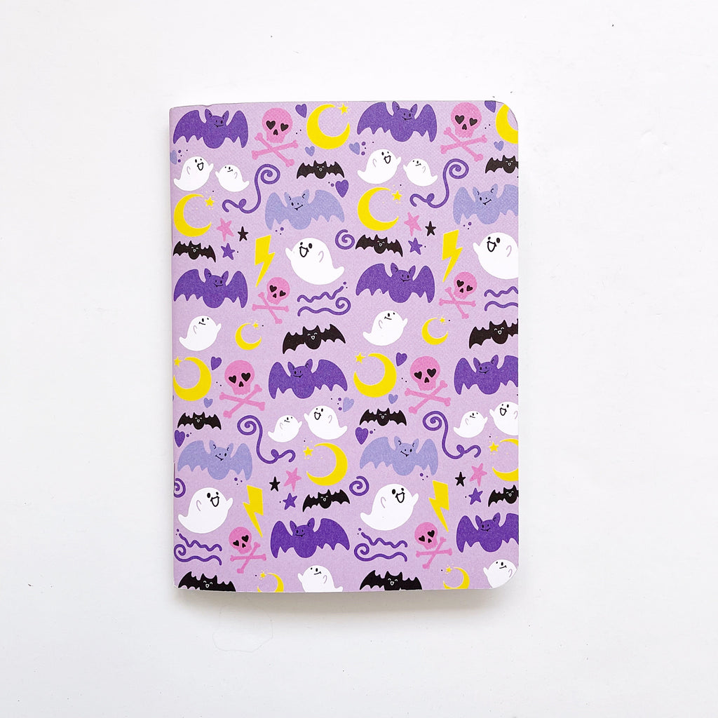 Image of notebook with lilac background and images of purple bats, white ghosts, yellow moons, pink skulls and black bats.