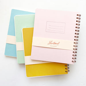 Image of four notebooks in pink, mustard, mint and blue with coiled binding on right side. 