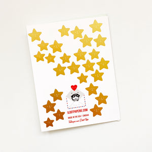 White card with several gold foil stars scattered on back of card. An envelope is included.