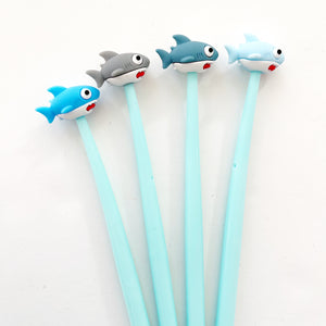 Image of four pens with pale blue barrels with sharks at the top of the pen. Bright blue shark with white underbelly and red mouth, light grey shark with white underbelly and red mouth, blue grey shark with white underbelly and red mouth and light blue shark with white underbelly with red mouth. 