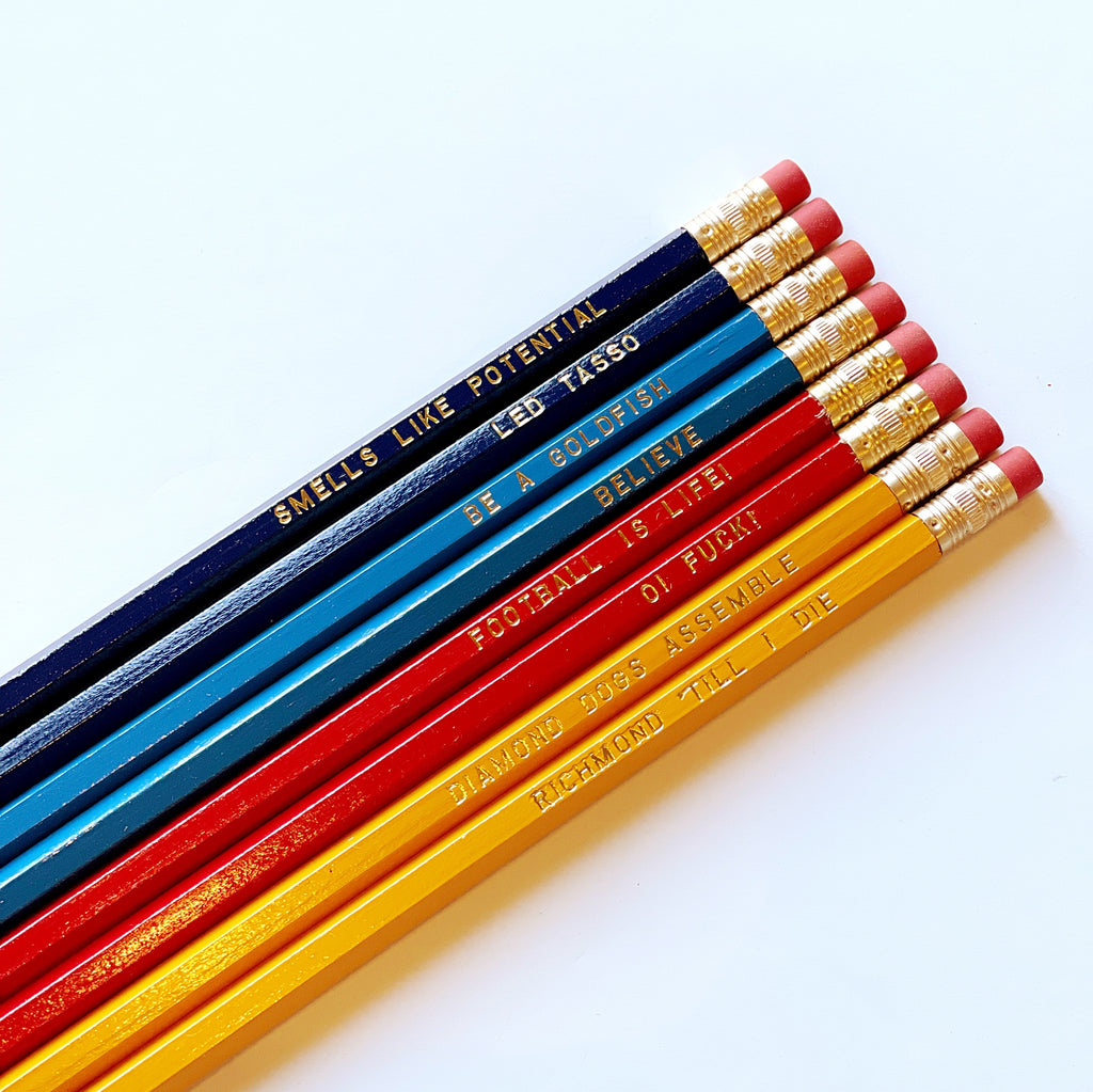 Image of set of pencils in dark blue, light blue, red and yellow with gold foil text says, "Smells Like Potential ","Led Tasso ","Be A Goldfish ","Believe", "Oi Fuck!", "Football Is Life", Diamond Dogs Assemble", Richmond Till I Die".