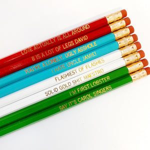 Eight pencils with gold text says, "Love Actually Is All Around, 8 Is A Lot Of Legs David, You're A Lonely, Ugly Asshole, I Hate Uncle Jamie! The ,Flashiest Of Flashes ,Solid Gold Shit Maestro!, I'm First Lobster,Say It's Carol Singers". 