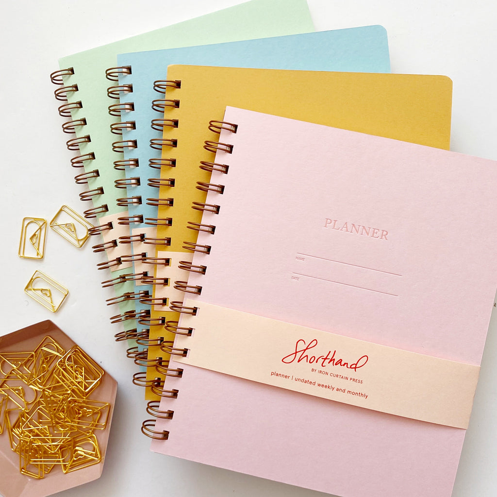 Image of planner covers in light pink, mustard, pool, and mint with side coiled binding. Letter pressed text says, “Planner”, “name” and “date” with lines for writing,