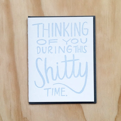 Ivory card with blue text saying, “Thinking of You During This Shitty Time”. A black envelope is included.